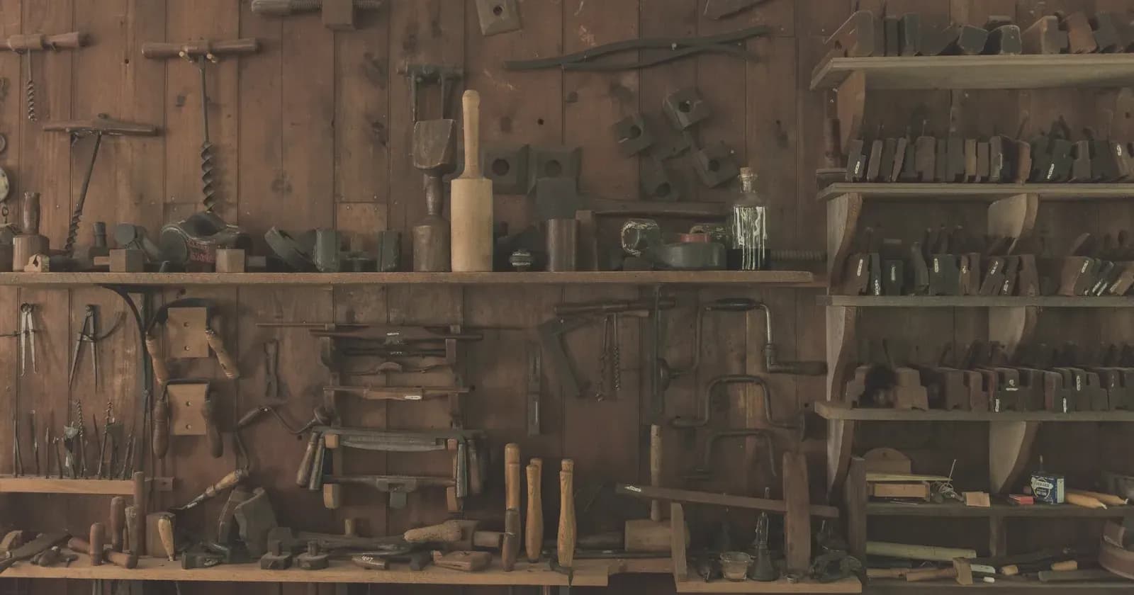 A workshop wall of assorted hand tools hung in rows on warm wooden racks.