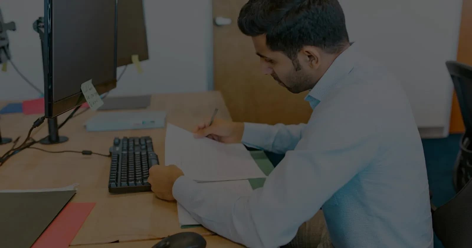 A professional at a desk reviewing a printed document, pen in hand, before signing.