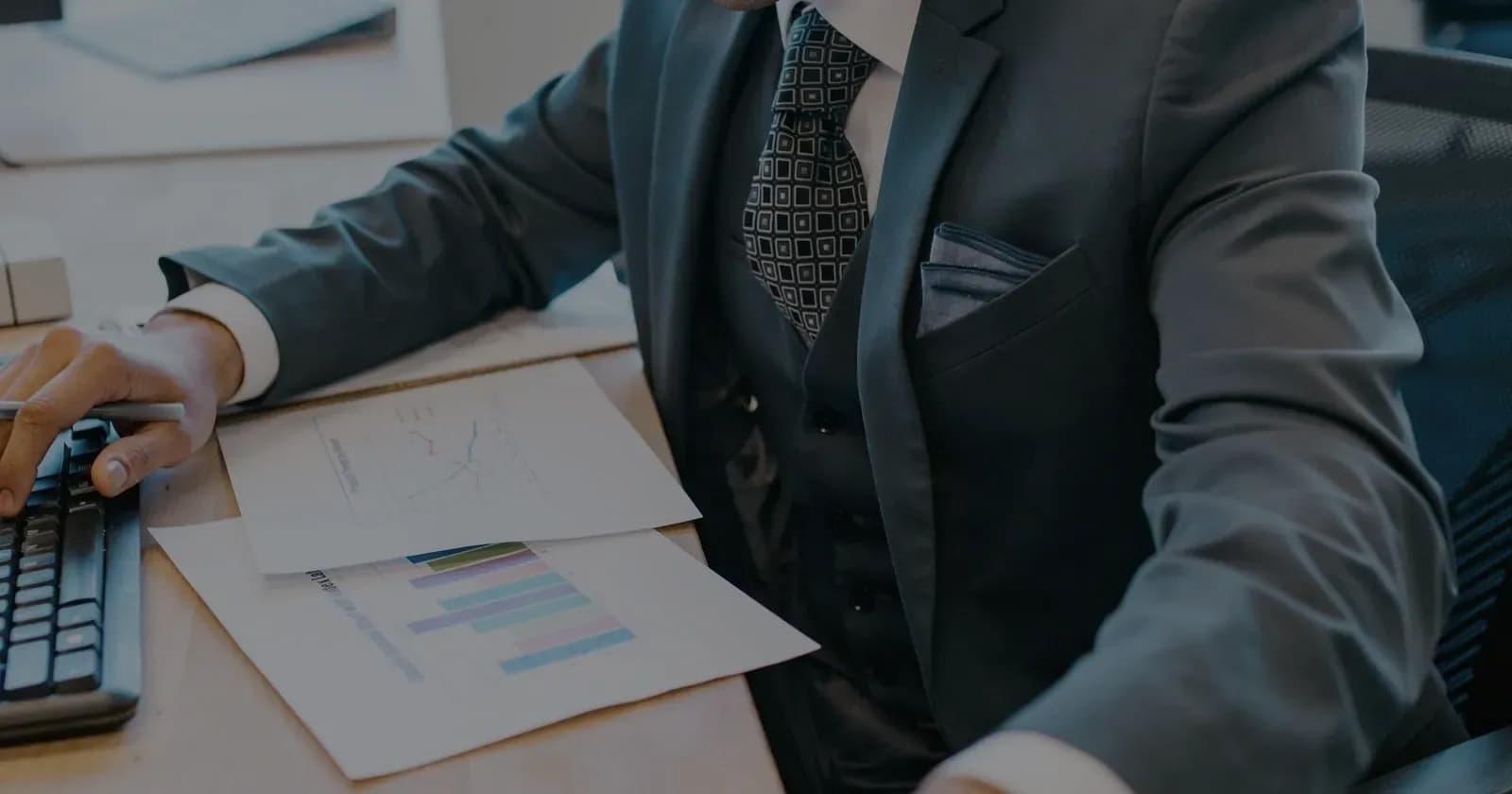 A professional at an office desk, hand resting on a calculator beside a printed bar chart and financial papers.