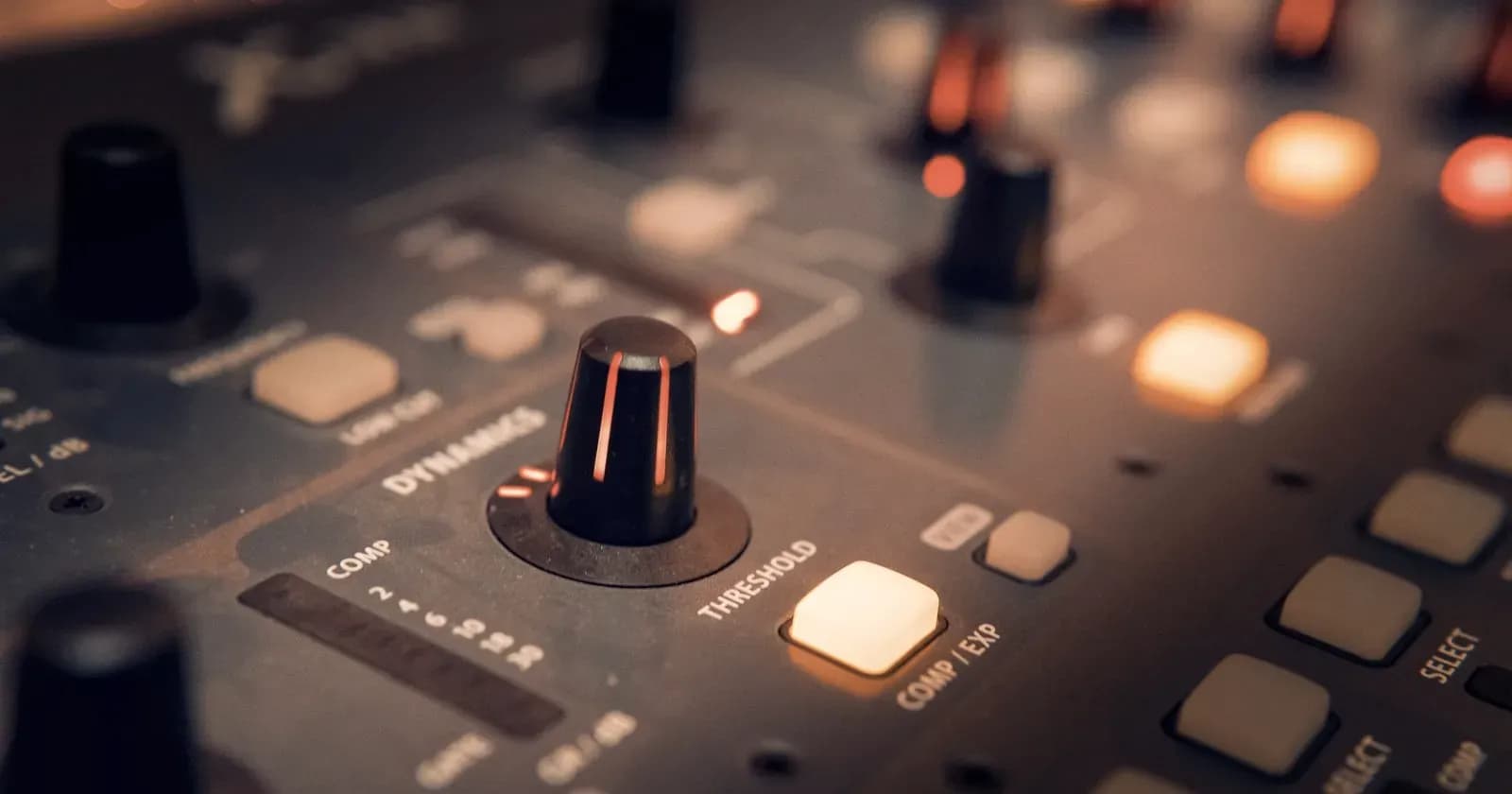 Close-up of a control console, rows of knobs and switches lit warm amber.