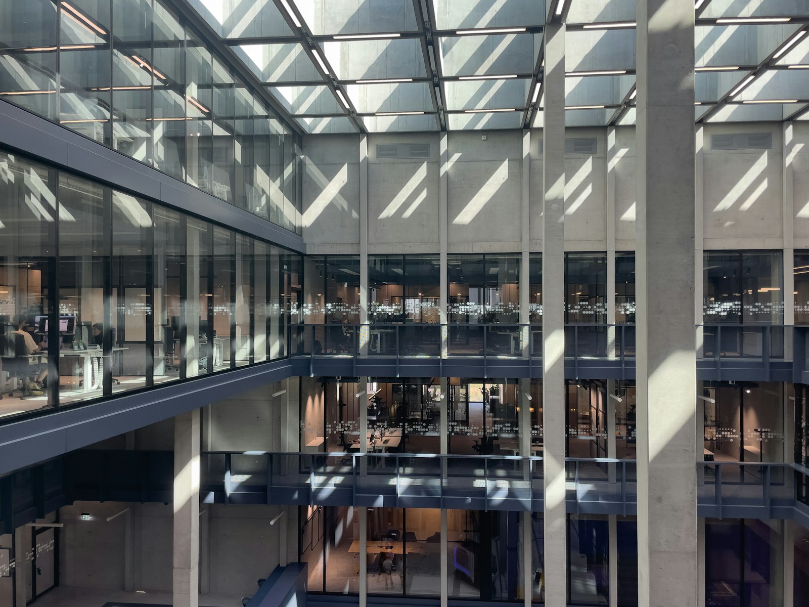 Modern glass-walled corporate office atrium with multi-storey workspaces visible through the facade