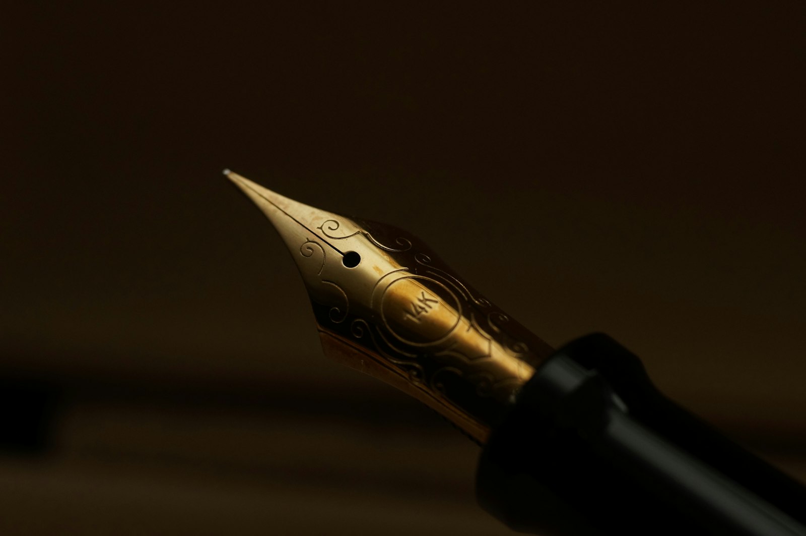 Close-up of a gold-engraved 14K fountain pen nib lit on a dark wooden desk