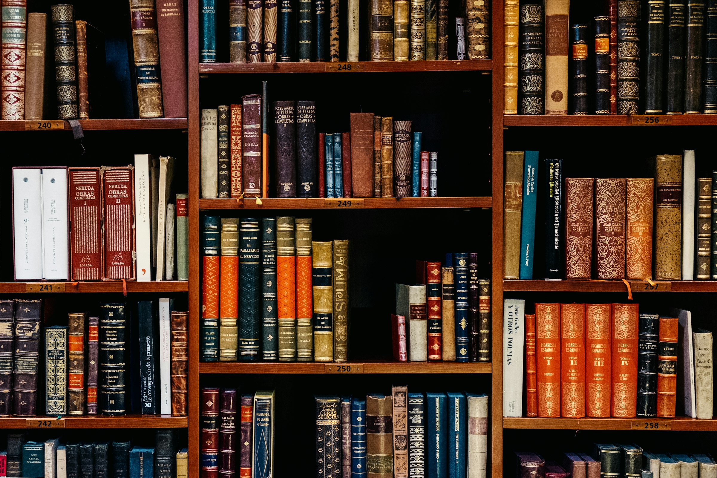 Densely-stacked old leather-bound books on warm wooden library shelves